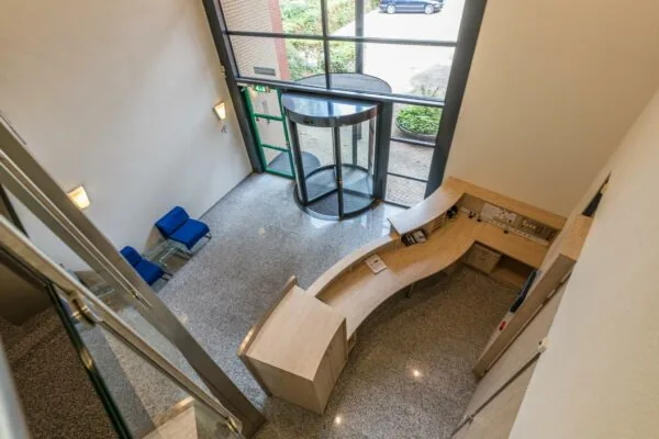 Moderne entreehal aan de Laan Blussé van Oud-Alblas met een houten receptiebalie, glazen draaideur en wachtstoelen.